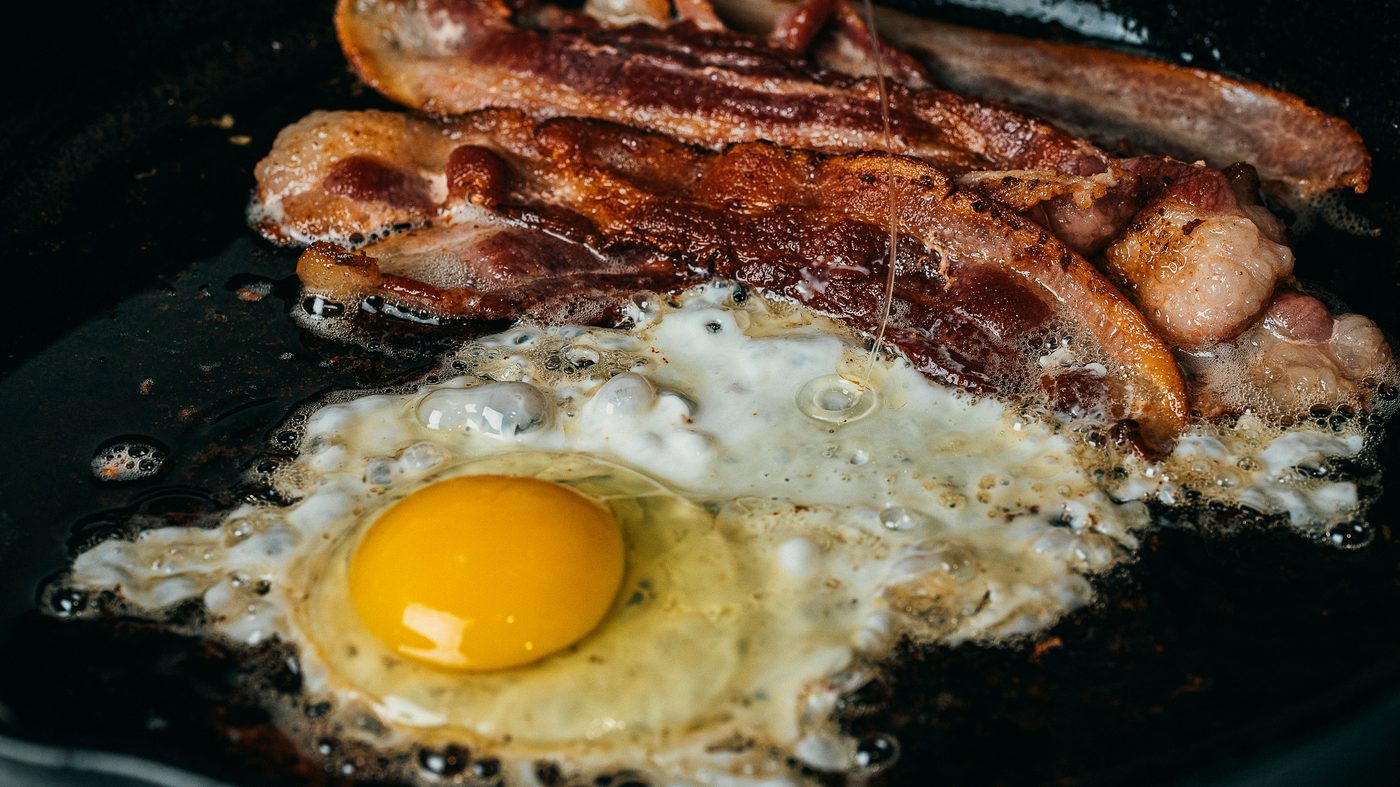Œuf au plat et tranches de bacon en train de griller dans une poêle en fonte noire
