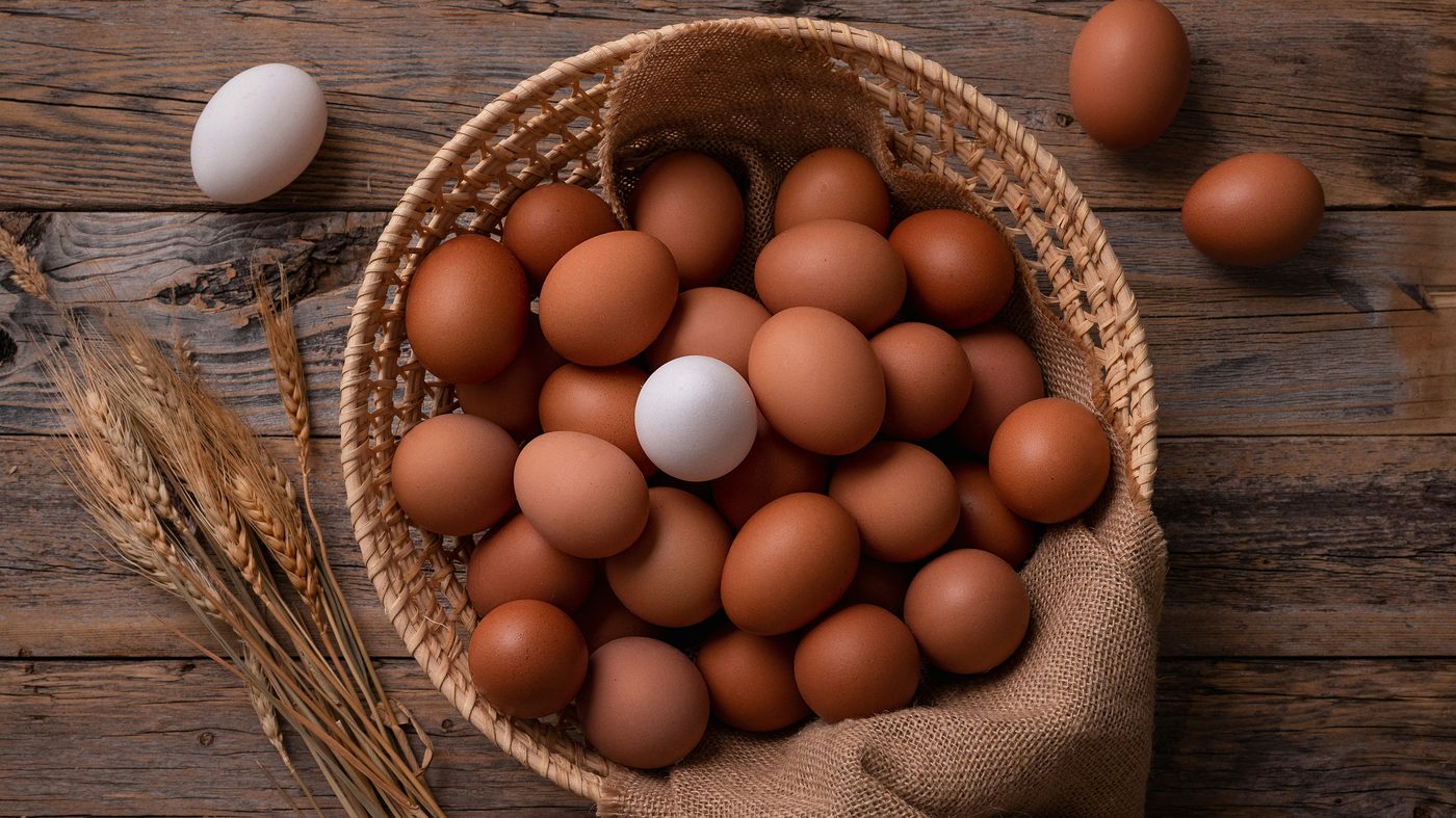 Œufs frais bruns et blancs dans un panier en osier posé sur une table en bois rustique