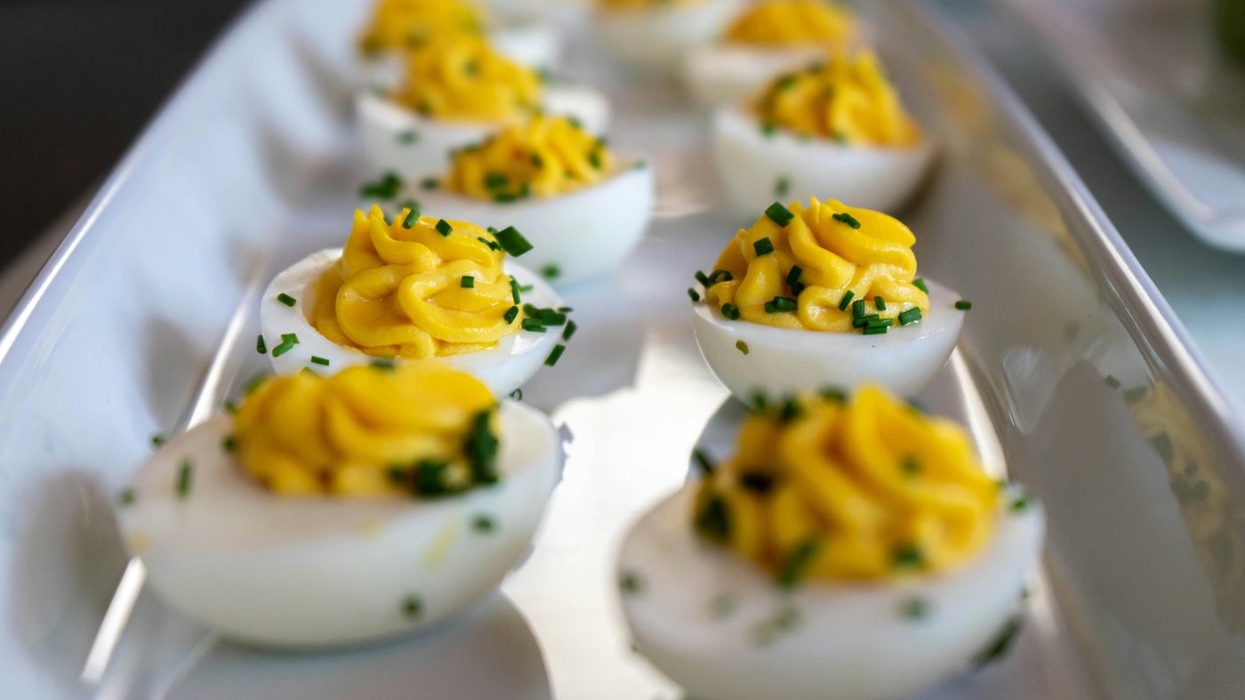 Œufs mimosa garnis à la poche à douille et parsemés de ciboulette, alignés sur un plat de service blanc