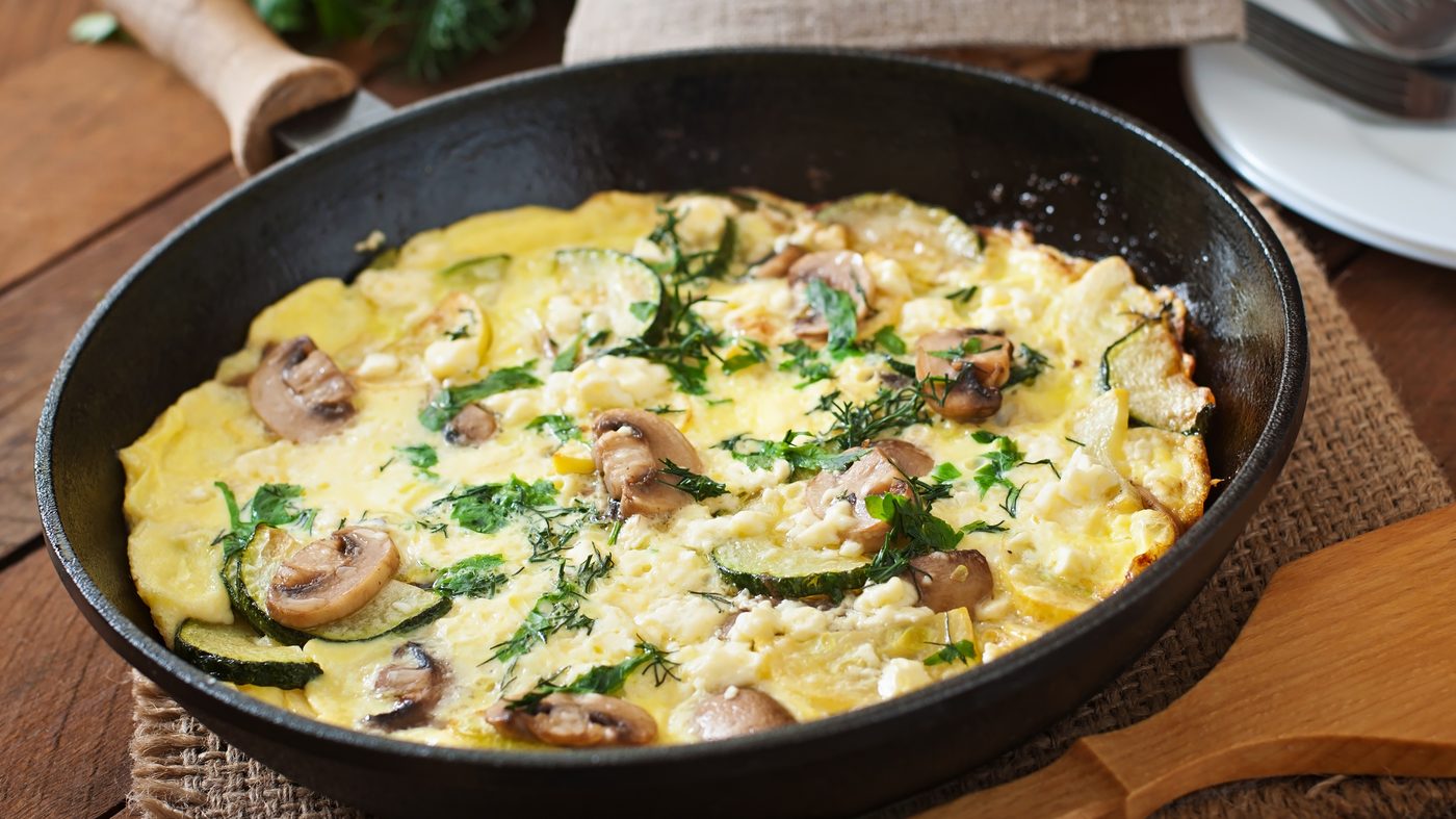 Omelette épaisse aux champignons, courgettes et fromage frais, cuite dans une poêle en fonte
